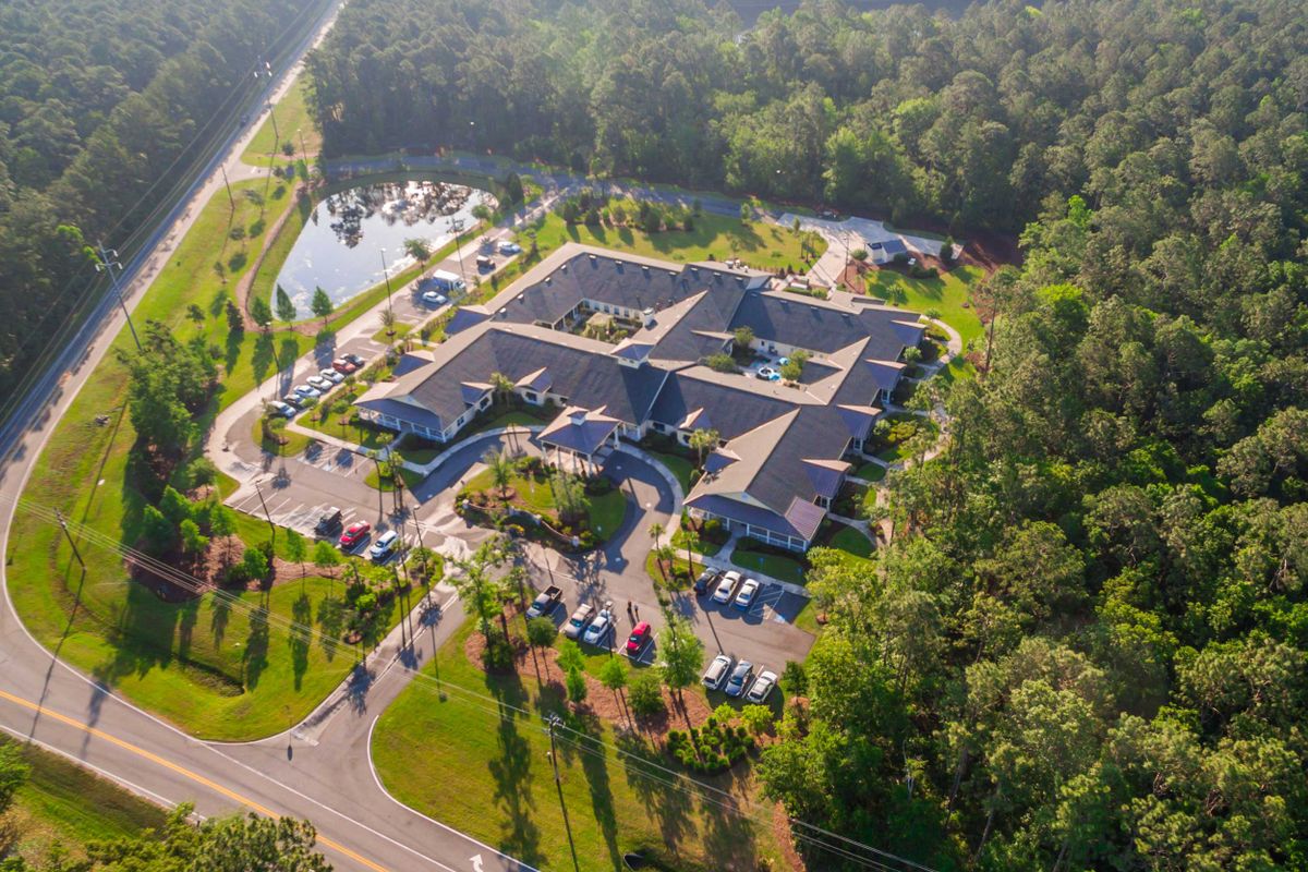 Aerial view of a large building complex surrounded by lush greenery and a parking area.