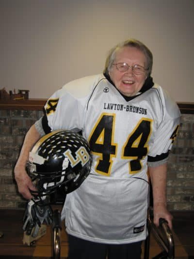 A person smiling while holding a football helmet and wearing a sports jersey.
