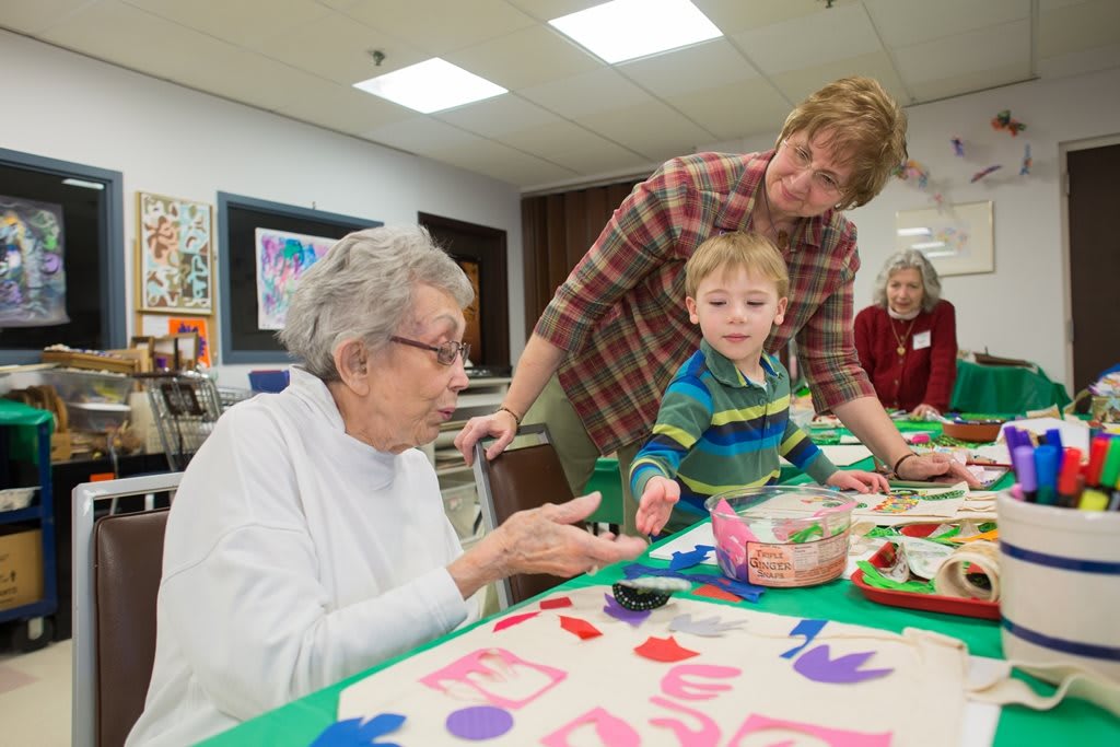 An elderly woman and a toddler engage in an intergenerational art activity together.