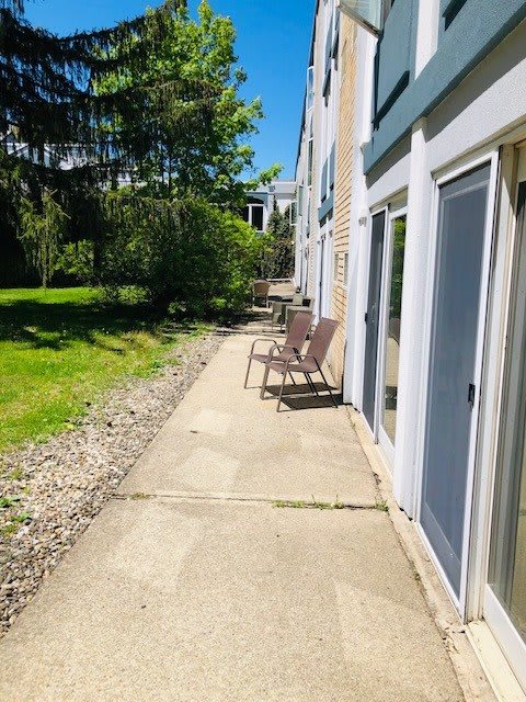 A sunny outdoor patio with chairs along a sidewalk adjacent to a building.