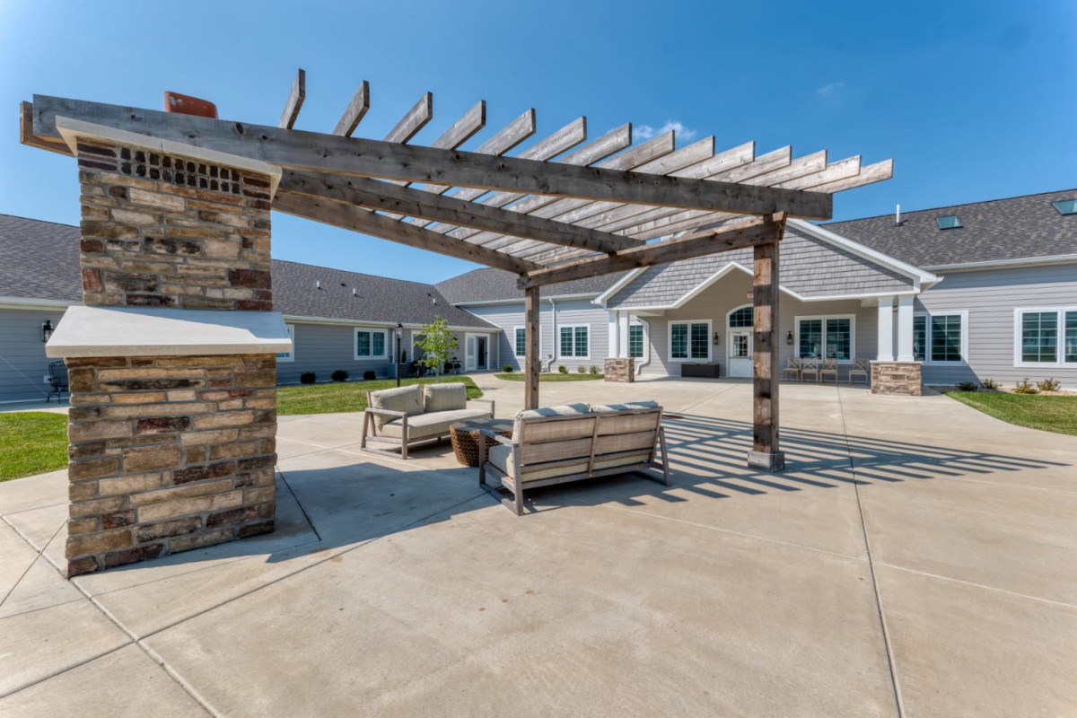 A sunny outdoor patio with a pergola and comfortable seating in front of a building.