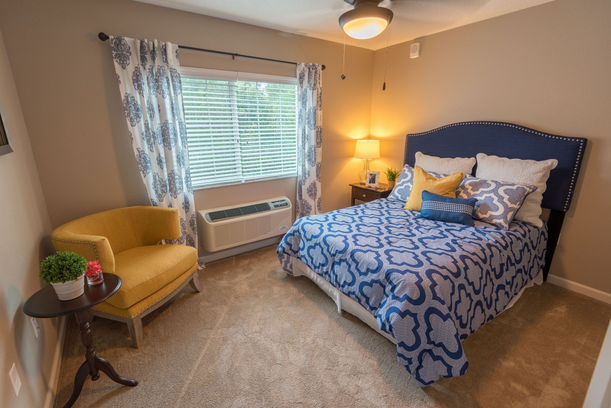 A cozy bedroom with a blue and white patterned bedspread, a yellow chair, and soft lighting.