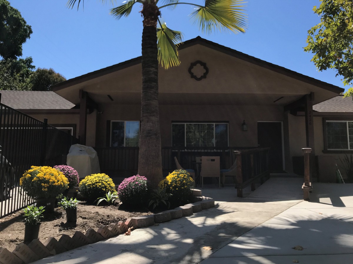 A sunny day view of a house with palm trees and colorful flowers in the front yard.