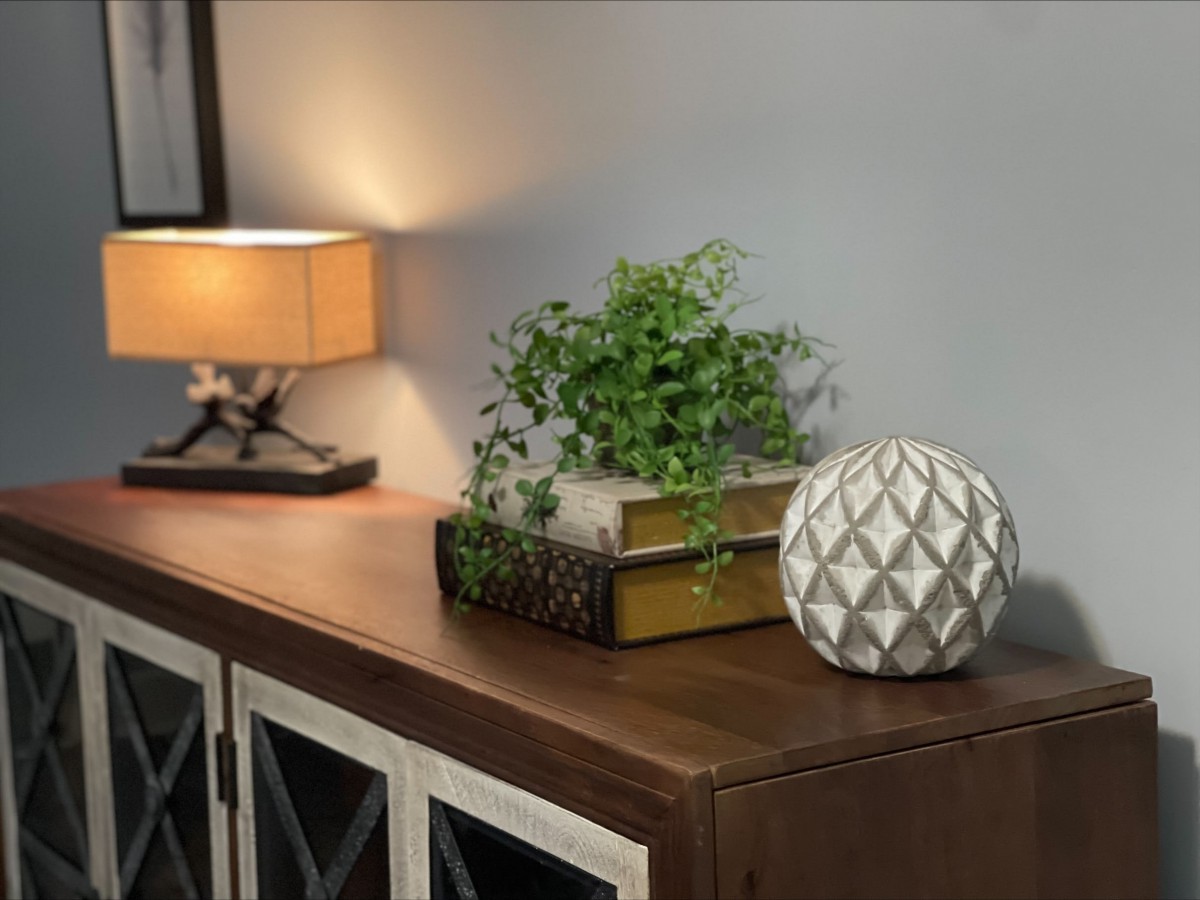 A cozy home interior with a warm-lit lamp, decorative plant, and books on a wooden cabinet.