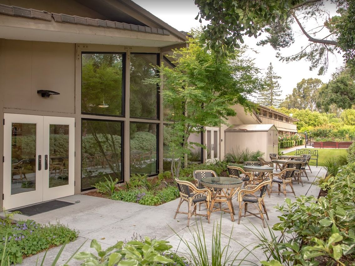 A peaceful outdoor seating area with tables and chairs surrounded by lush greenery beside a building.