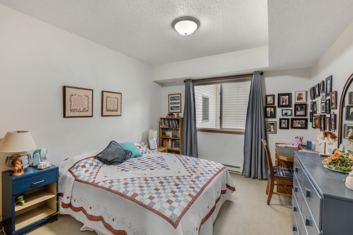 A cozy bedroom with a bed, wall artwork, a bookshelf, and a desk near the window.