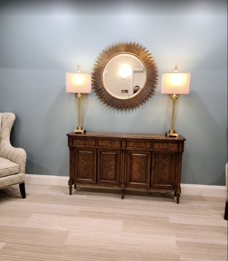 A stylish living room features a wooden cabinet with a circular mirror and two elegant lamps, complemented by plush armchairs on either side.