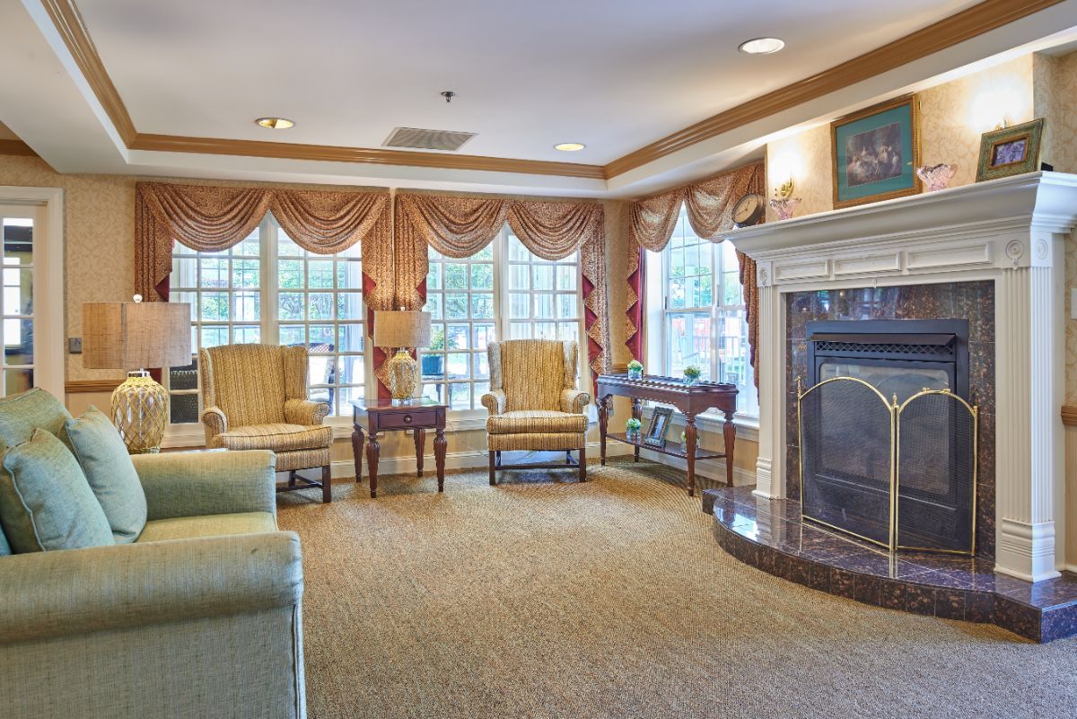 A cozy living room with a fireplace, armchairs, and large windows adorned with curtains.