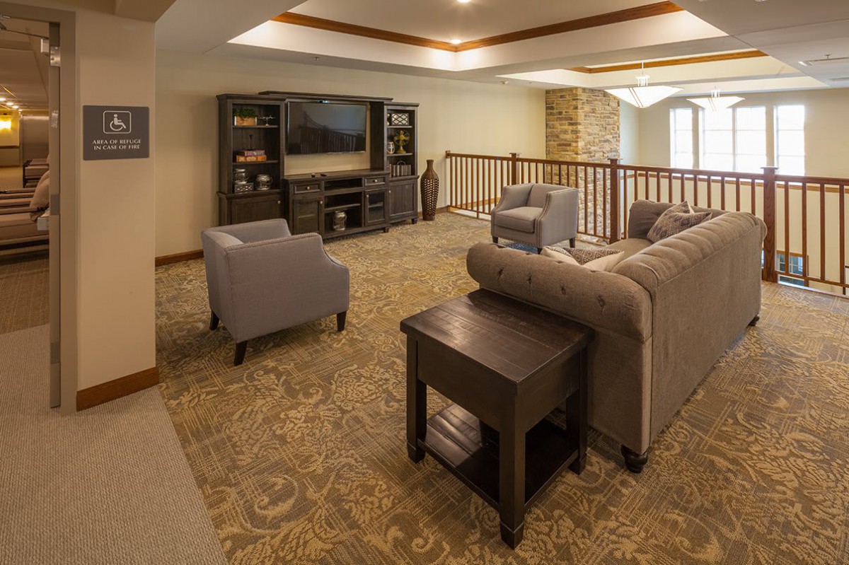 A cozy living room with a sofa, armchairs, and a television set against wooden shelving.