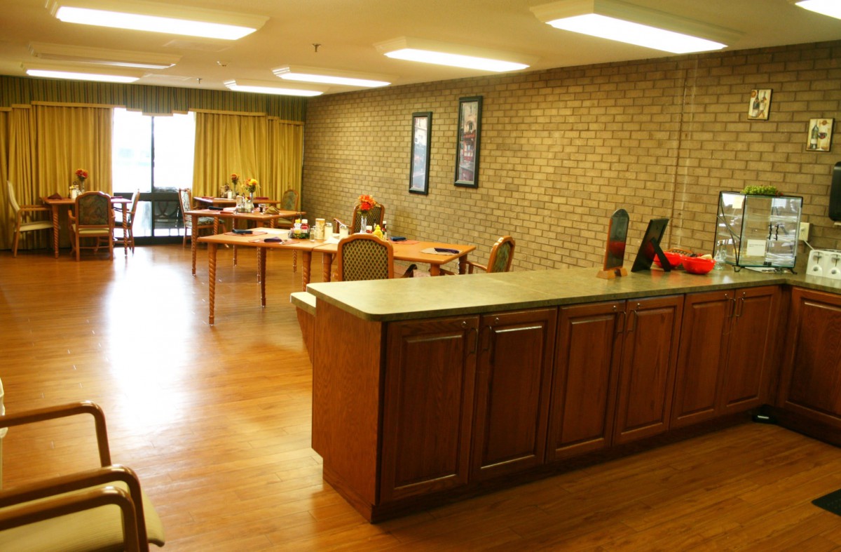A view of an office workspace with multiple desks and chairs, featuring a brick wall and wooden flooring.