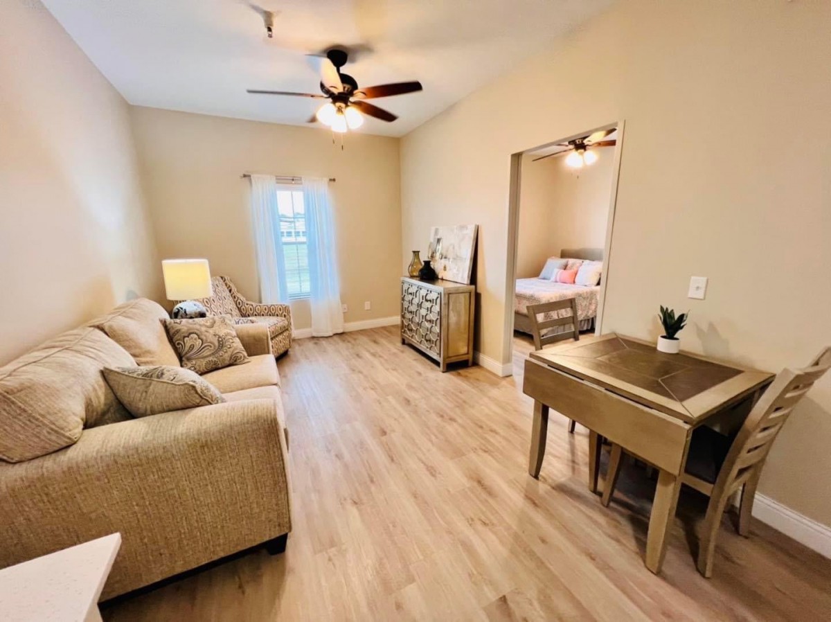 A bright and cozy living room with comfortable sofas, a ceiling fan, and wood flooring.