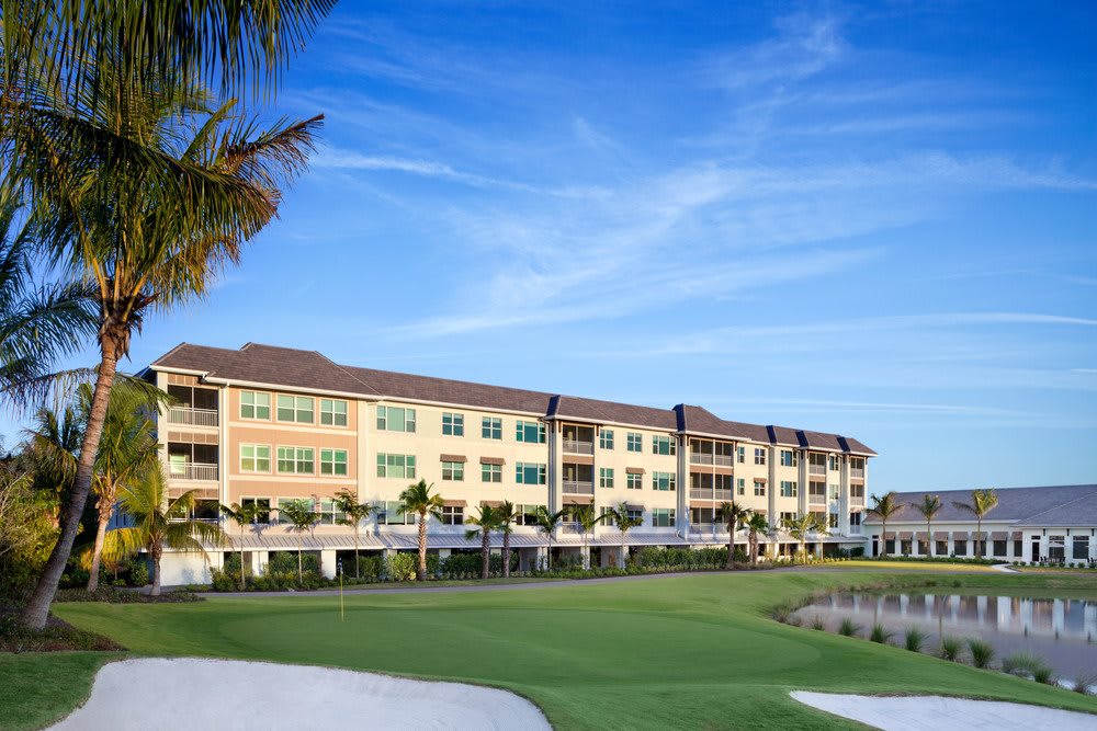 A luxurious resort building next to a manicured golf course under a bright blue sky.