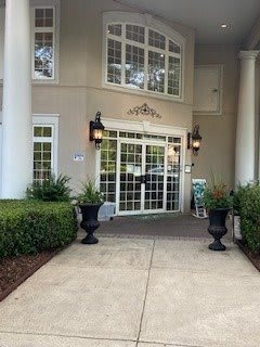 Entrance of a building with columns and landscaped shrubs.