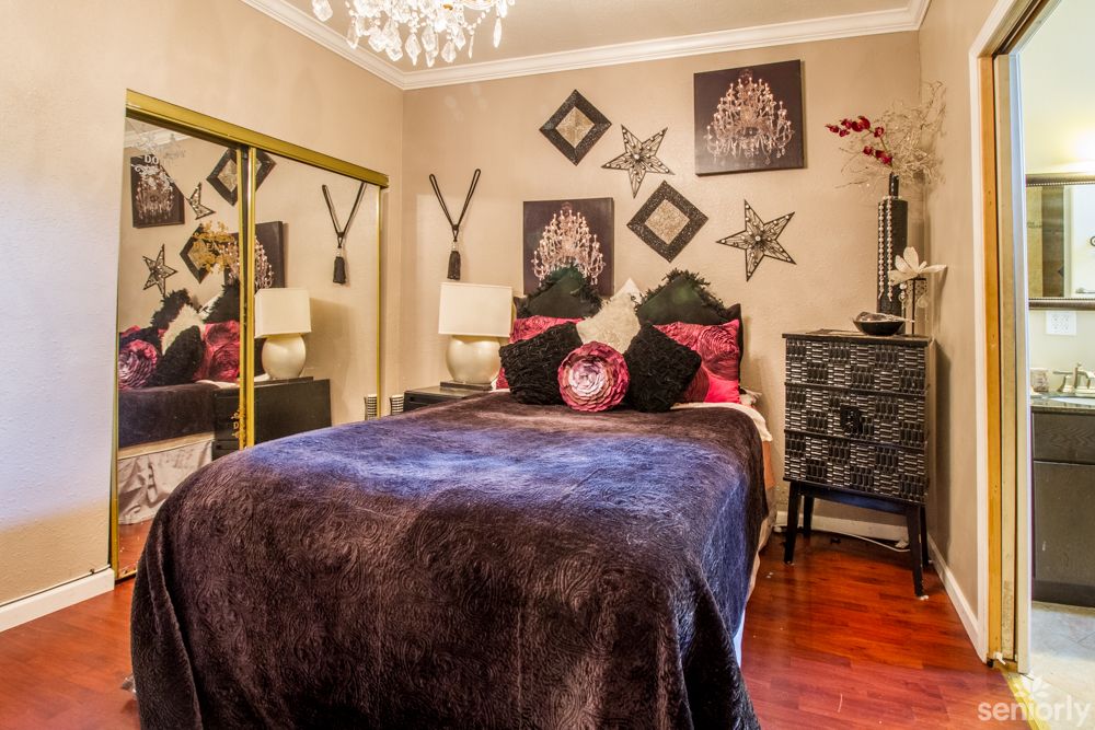 A well-decorated bedroom featuring a cozy bed with plush bedding, mirrored closet doors, and artistic wall decor.