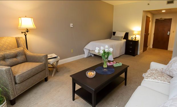 A cozy bedroom featuring a single bed, a coffee table with decorative items, and soft lighting from a bedside lamp.