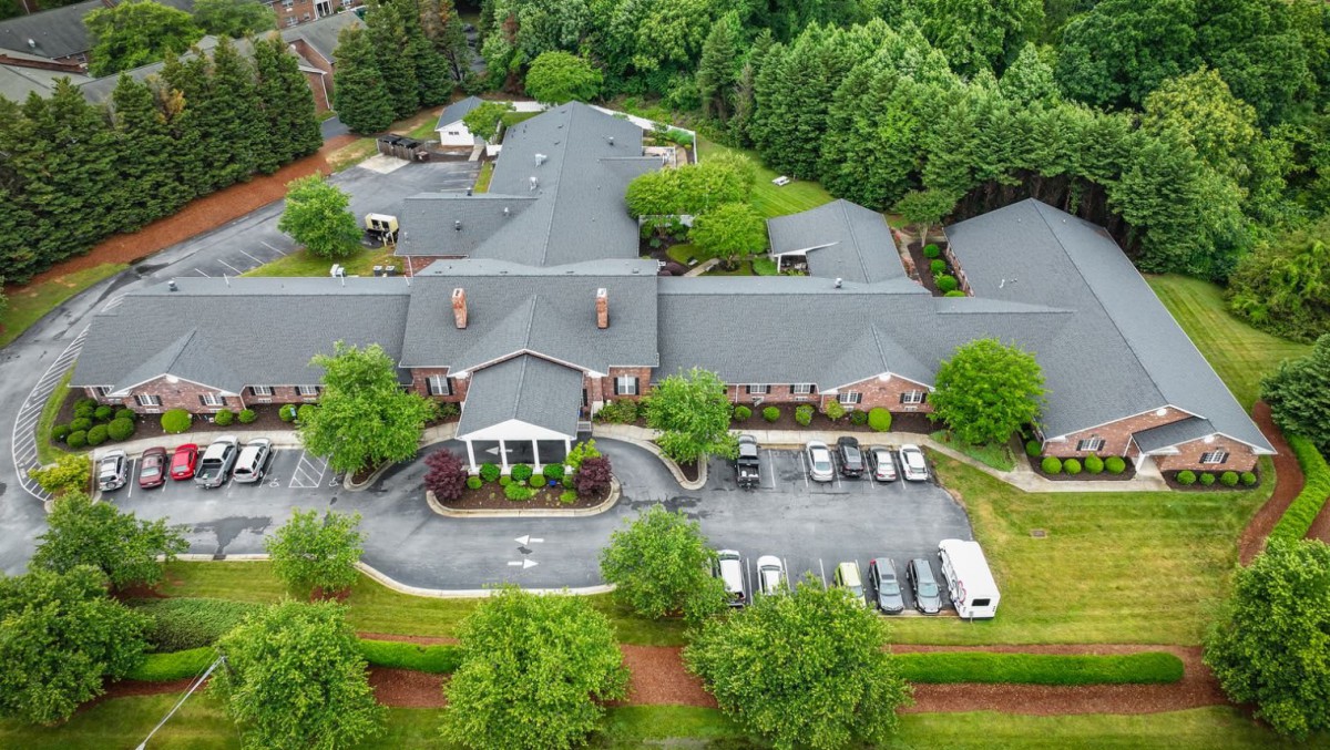 Aerial view of a large building surrounded by trees with a parking lot in front.