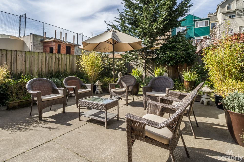 A cozy outdoor patio with wicker furniture set and a large sun umbrella in a sunny garden setting.