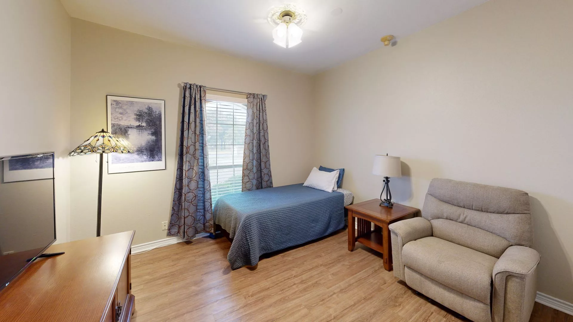A cozy bedroom with a single bed, armchair, and wooden flooring.