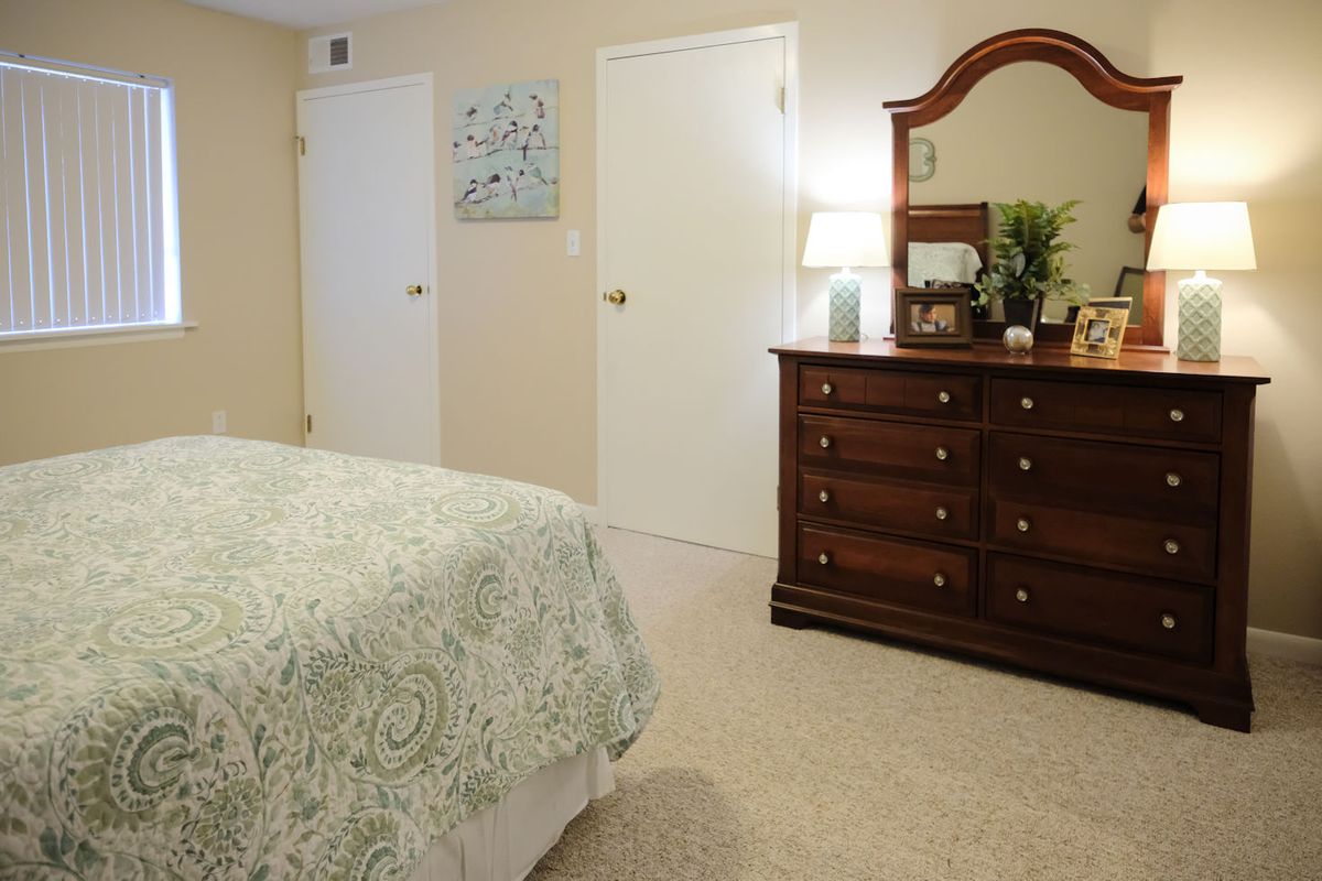 A cozy bedroom featuring a patterned bedspread, a dresser with a mirror, and decorative elements.