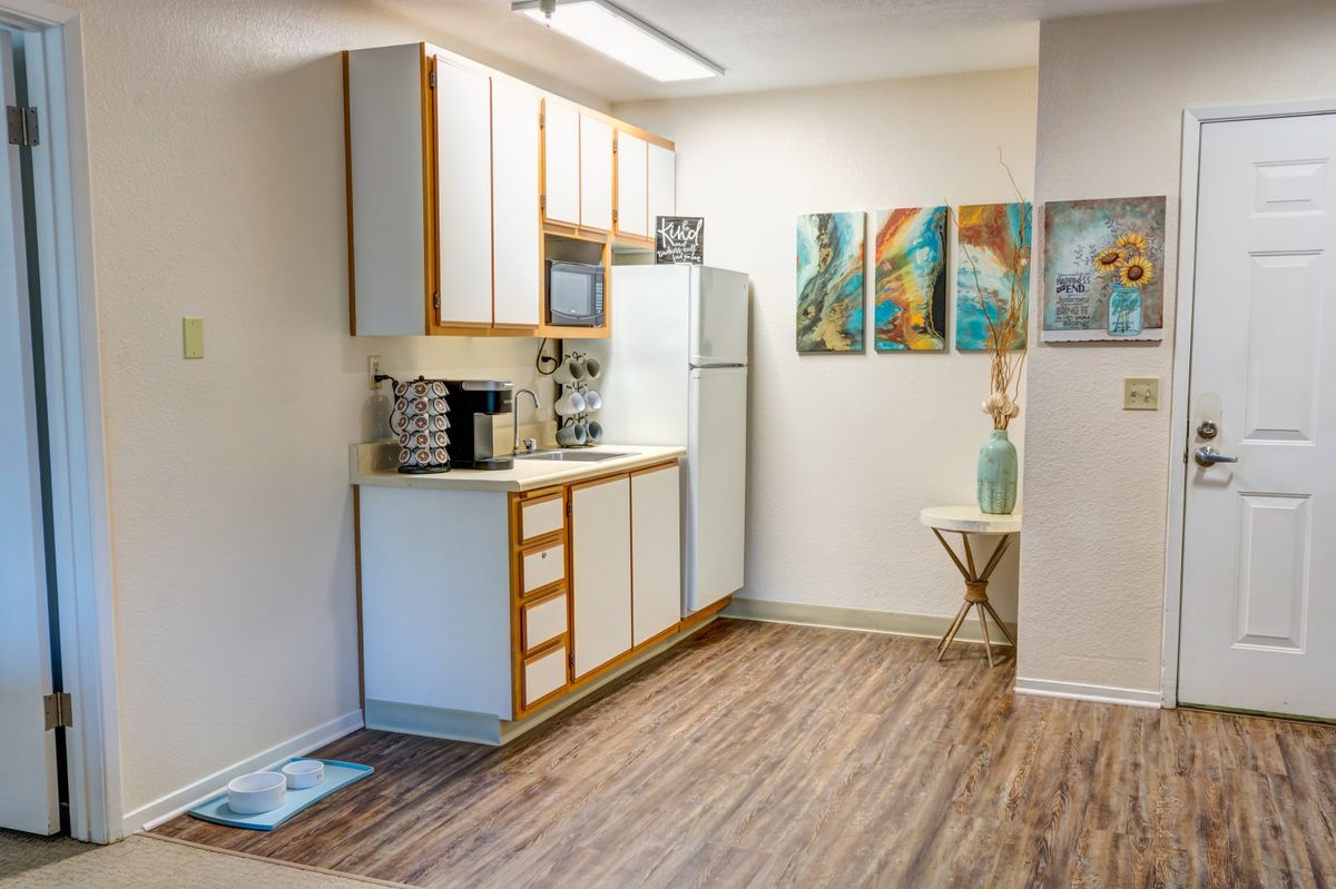 A modern kitchen interior with white cabinets, wood flooring, and colorful artwork on the wall.