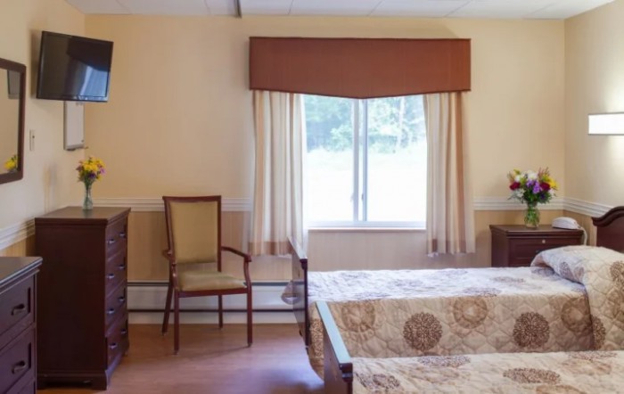 A cozy bedroom featuring a window with curtains, a chair, and a bed with patterned bedspread.