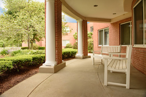 A serene porch with a bench, surrounded by greenery and elegant columns.