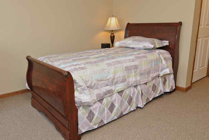 A neatly made bed with a wooden frame and a lamp on a bedside table.