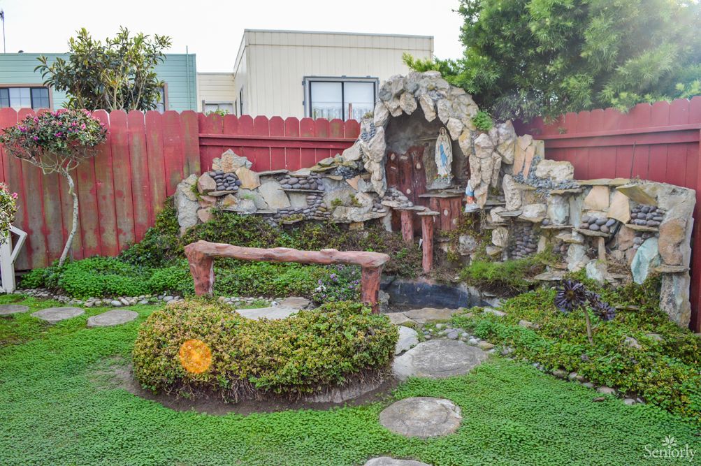 A serene garden with a small shrine and lush greenery, surrounded by a red wooden fence.