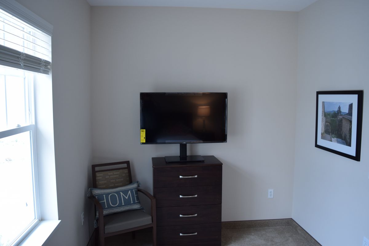 A minimalist room setup with a television on a dresser and a chair with a pillow.