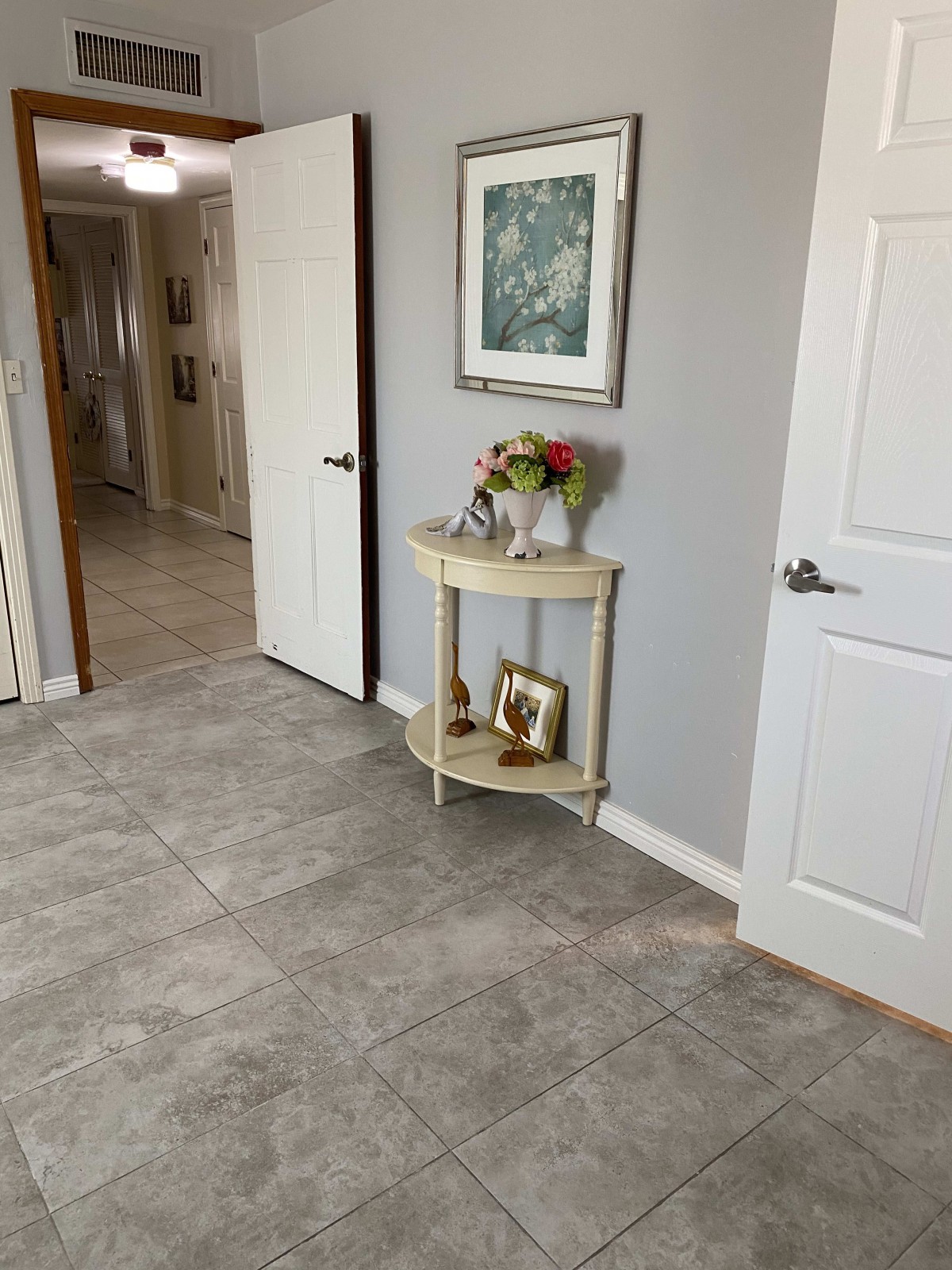 A tidy hallway with a small table displaying flowers, photographs, and artwork on the wall.
