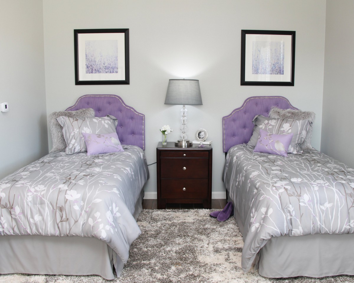 A bedroom with twin beds featuring purple accents and a central nightstand.
