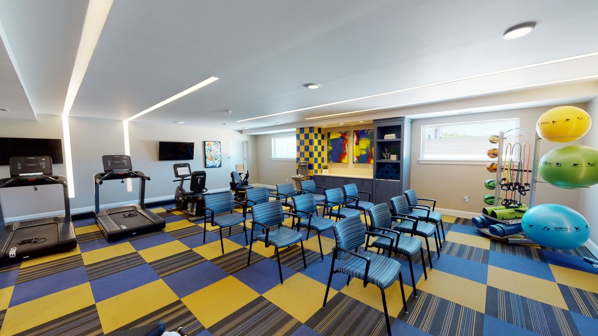 A multi-purpose room featuring arranged chairs, treadmills, and colorful artwork on the walls.