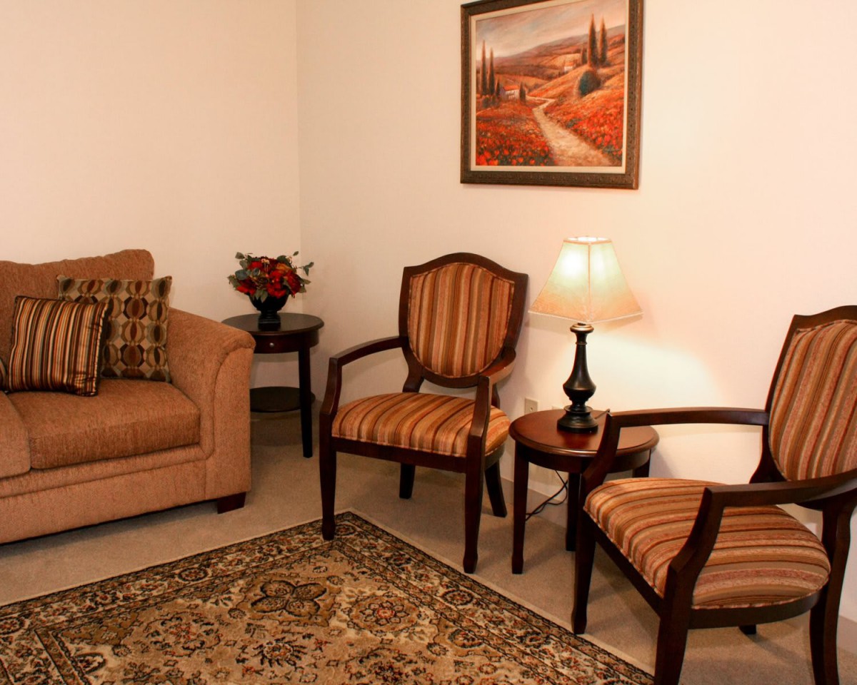 A cozy living room with a sofa, two chairs, a table lamp, and a decorative painting on the wall.