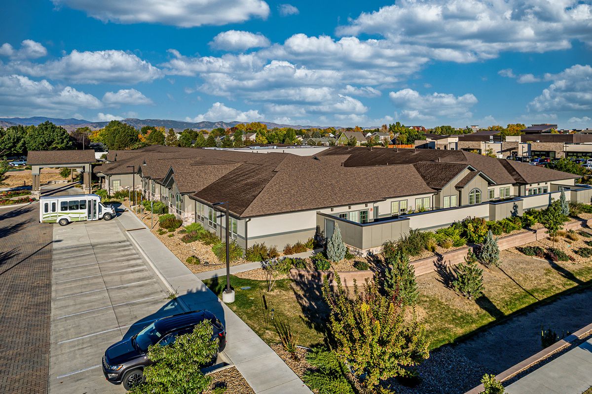 Aerial view of residential buildings with a parking lot and surrounding greenery under a cloudy sky.