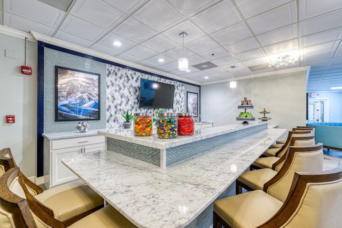 A modern kitchen with a marble bar counter and seating, featuring beverage jars and fruit displays.