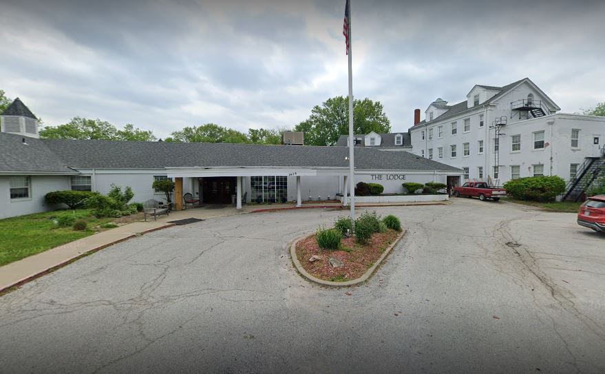 A facility entrance with a driveway and flagpole under a cloudy sky.