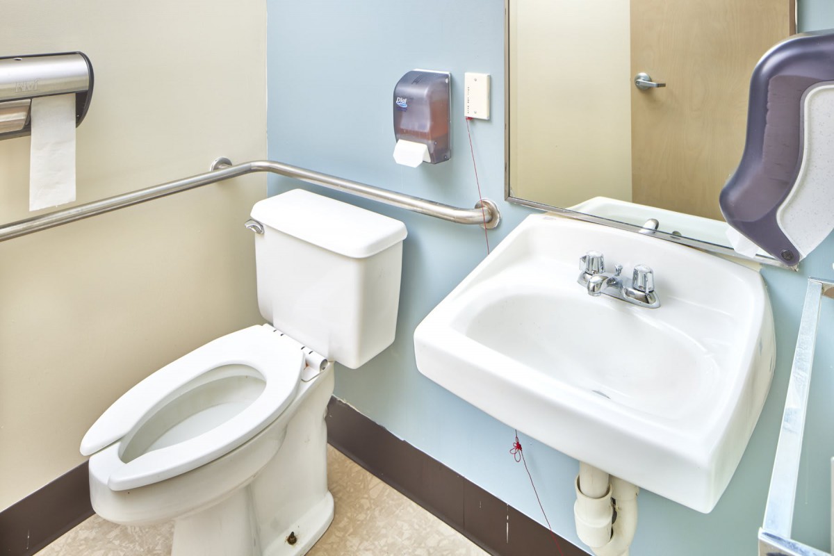 A public restroom featuring a toilet, sink, mirror, and handrail.