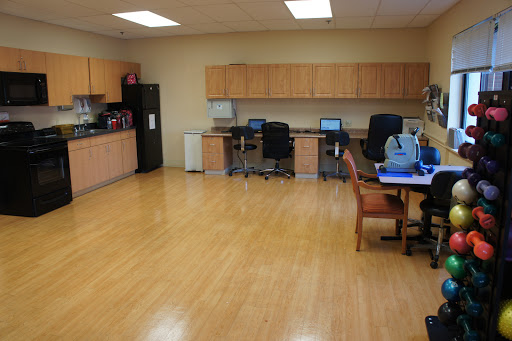 A spacious office area featuring a kitchenette, workstations with computers, and comfortable seating.