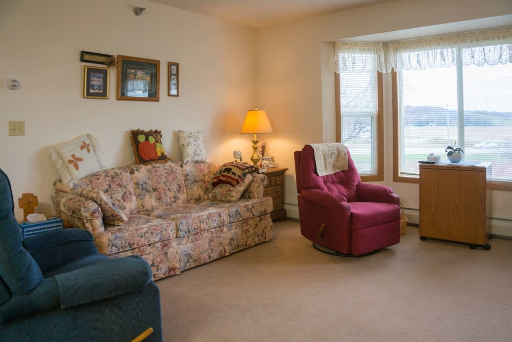 A cozy living room with a floral sofa, red armchair, and a lamp by the window.