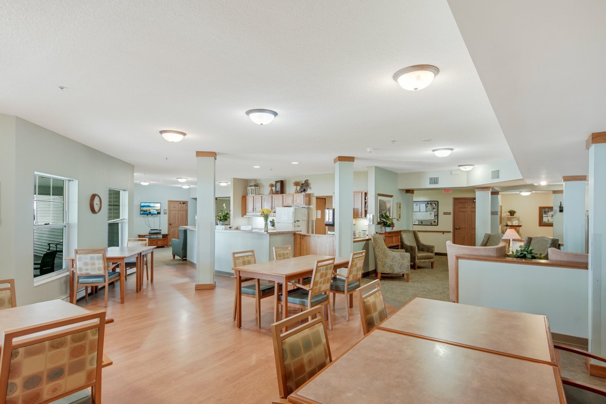 A spacious dining area with wooden floors and modern lighting, featuring multiple tables and chairs.