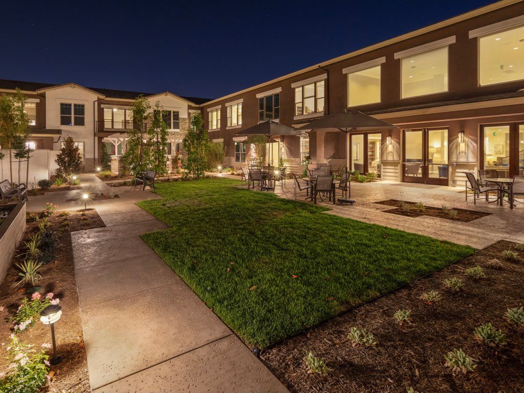 A beautifully lit mansion exterior at night, showcasing modern architecture and a well-maintained landscape.