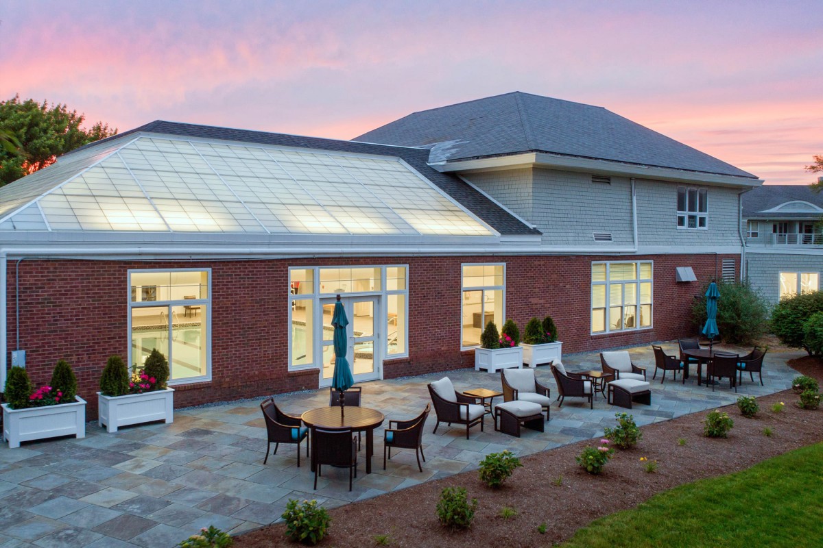 A modern building with an outdoor patio area featuring brick exterior walls, table and chairs set under a sunset sky.