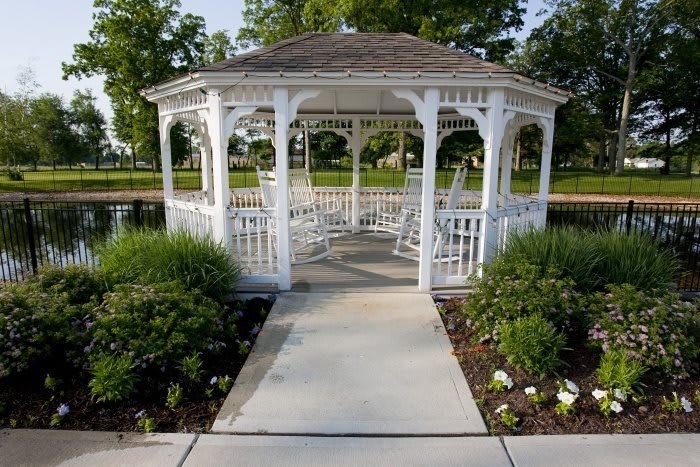 A white gazebo surrounded by greenery and a paved pathway in a garden setting.