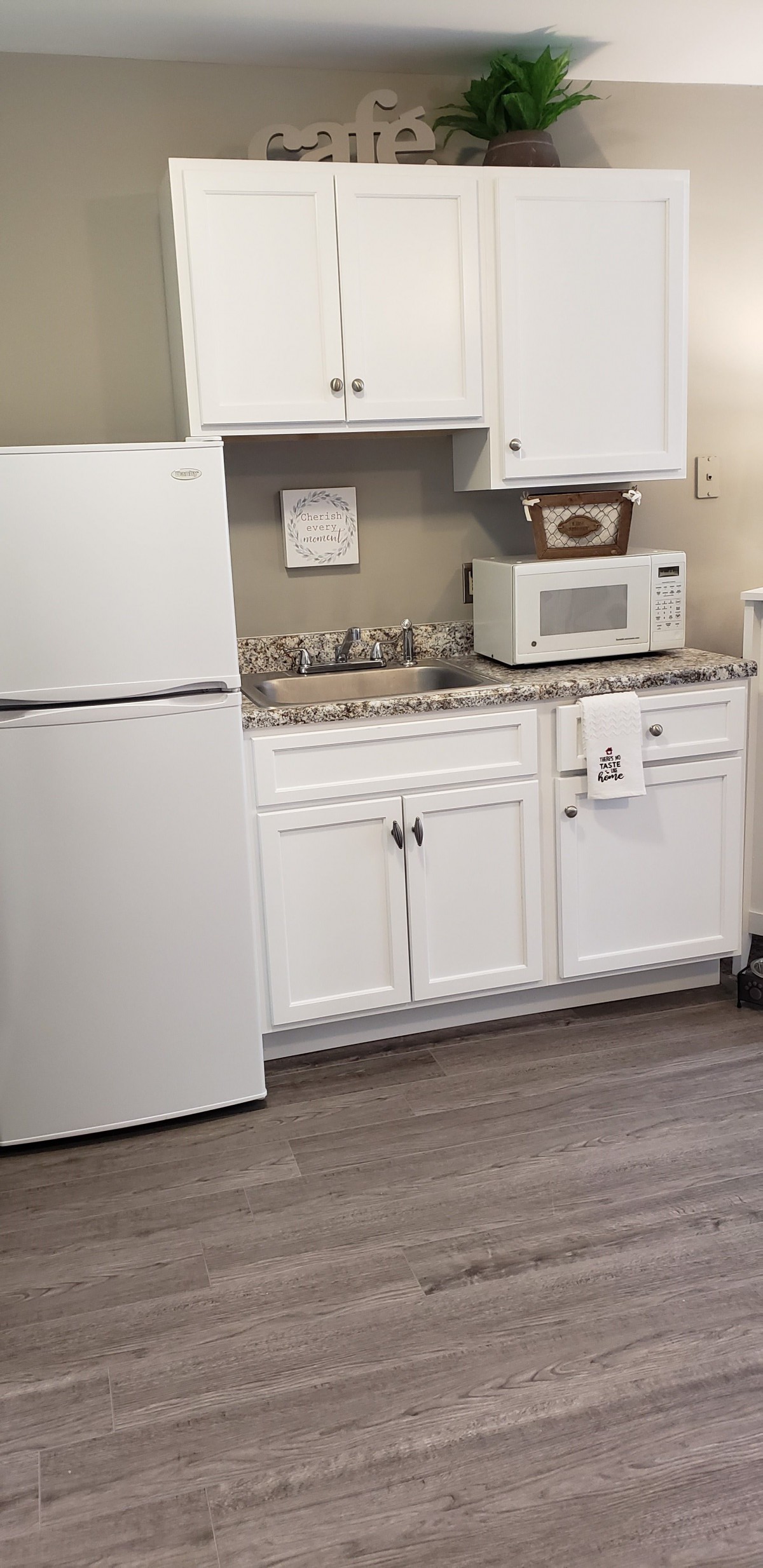 A compact kitchen area with a refrigerator, microwave, and white cabinetry.