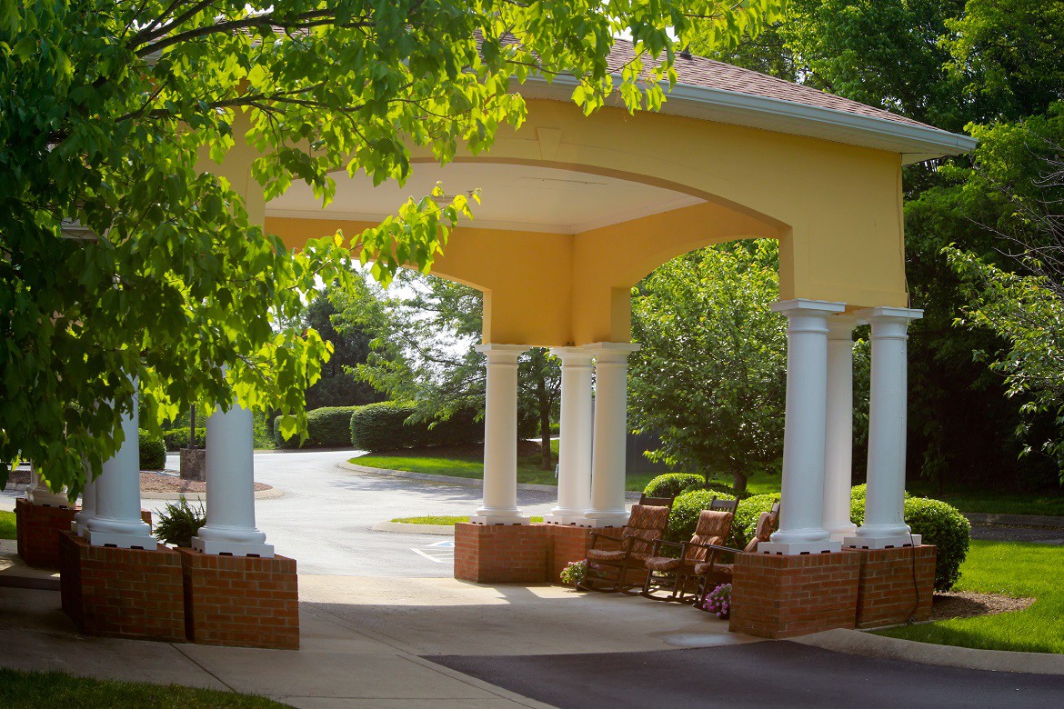 An outdoor entrance with columns, featuring a landscaped driveway and surrounding greenery.