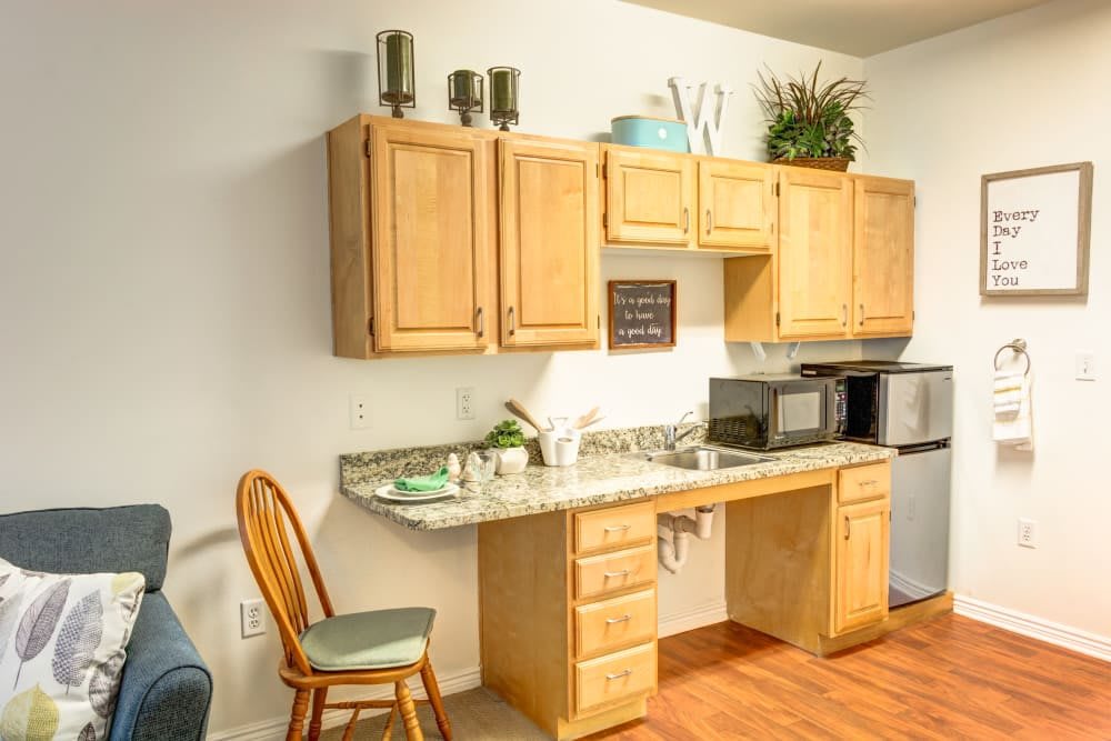 A small kitchen area with wooden cabinets and a granite countertop, featuring a microwave and decorative items.