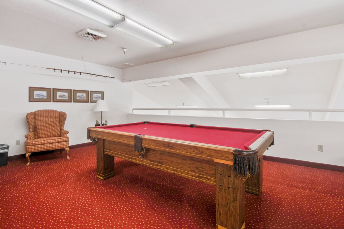 A cozy billiard room featuring a pool table with a red felt surface, complemented by a red carpet and classic decor.
