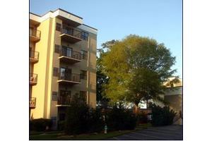 A residential apartment building with balconies and a large tree nearby, captured at sunset.