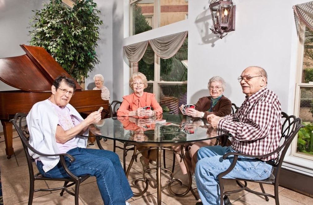 A group of seniors sitting around a table playing cards in an indoor setting.