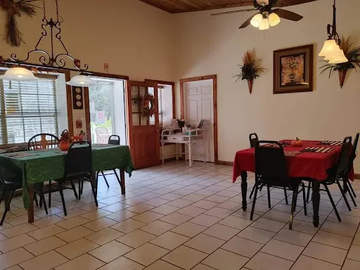 A cozy dining area featuring two tables set with colored tablecloths, surrounded by chairs and adorned with wall decorations.